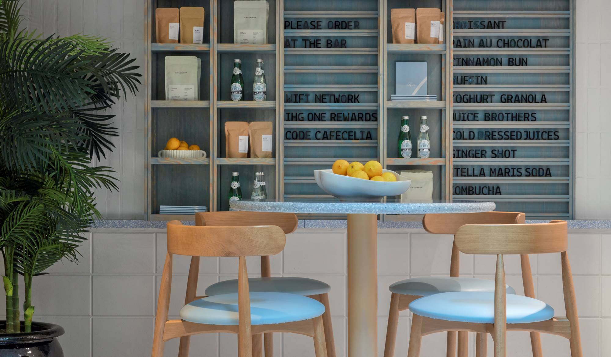 A modern café corner with a menu board, plant, and a table set with drinks and snacks at Café Celia in Amsterdam.