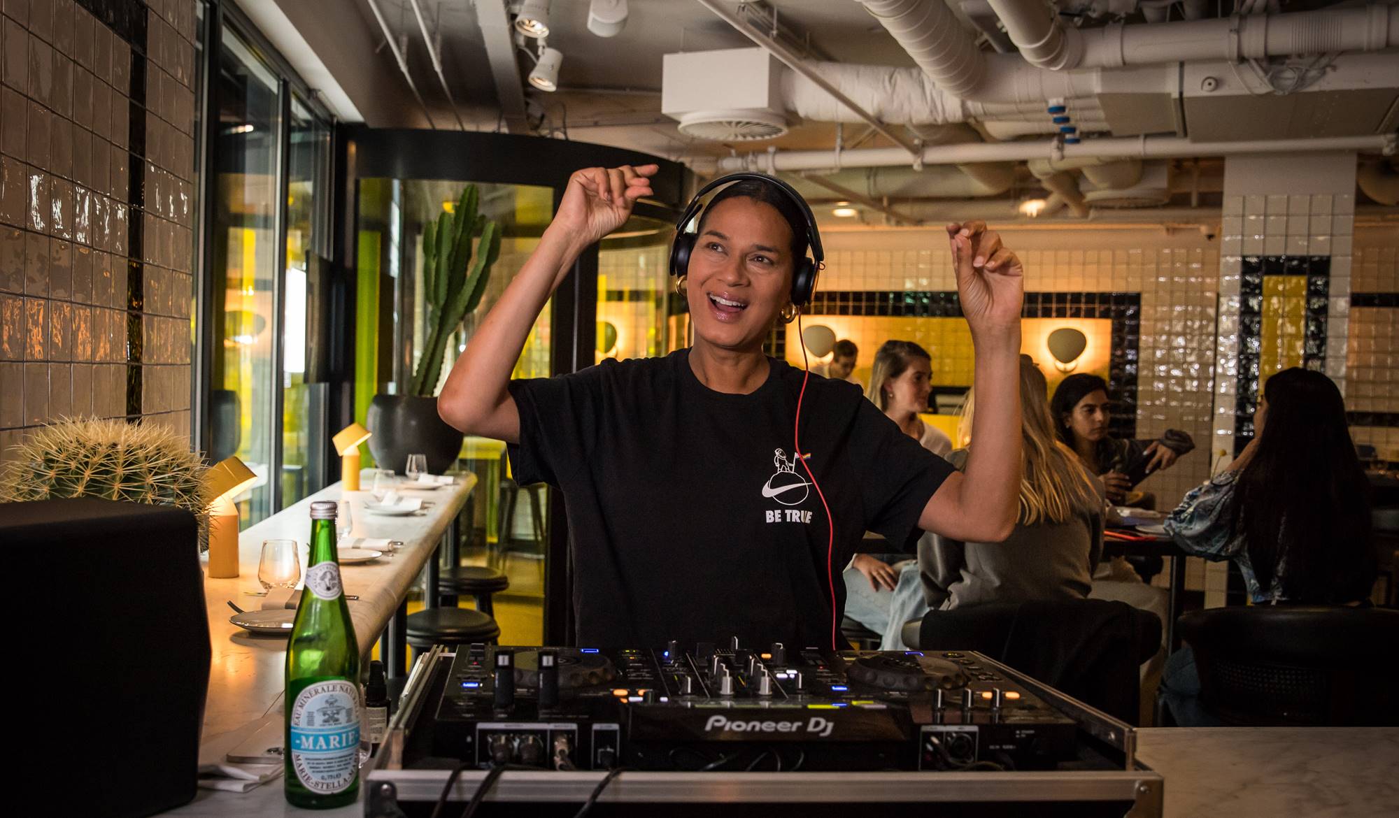 A DJ in headphones spins music, creating a lively atmosphere in Celia's vibrant setting for DJ Fridays in Amsterdam.