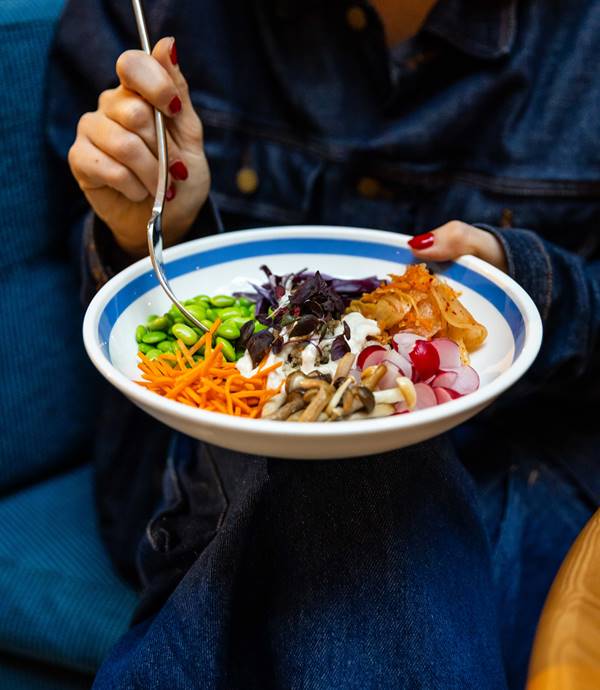 A bowl filled with fresh vegetables, edamame, kimchi, and mushrooms being held by a woman at Celia restaurant in Amsterdam.