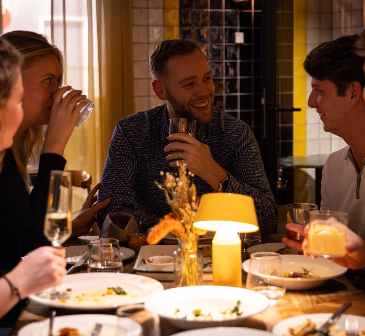 A group of friends laughing and enjoying drinks together at a table at Celia restaurant in Amsterdam.