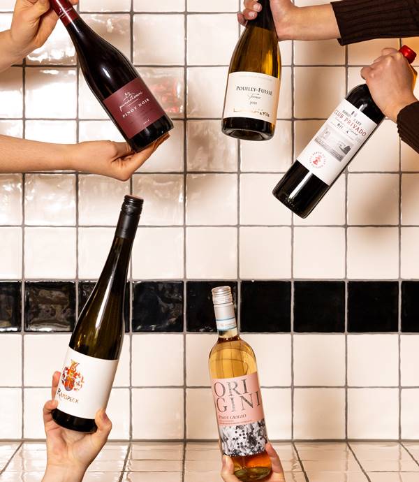Multiple bottles of wine held up, including red, white, and rosé varieties with a white tiled background at Celia Amsterdam.