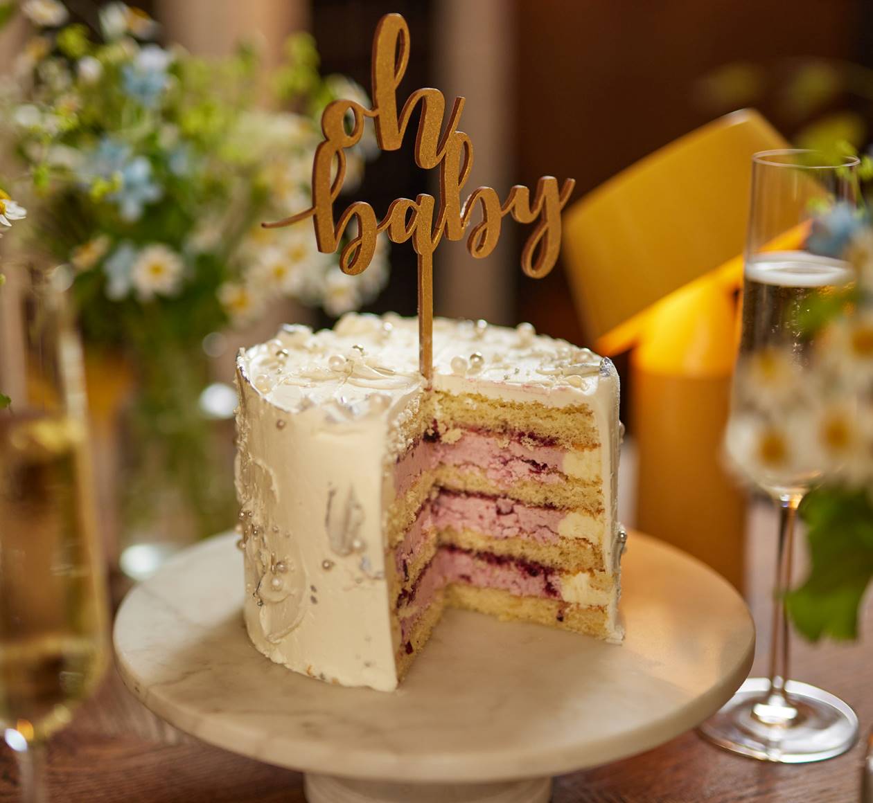 A decorated "Oh Baby" cake with pink filling and white icing, flowers and drinks at a baby shower at Celia Amsterdam.