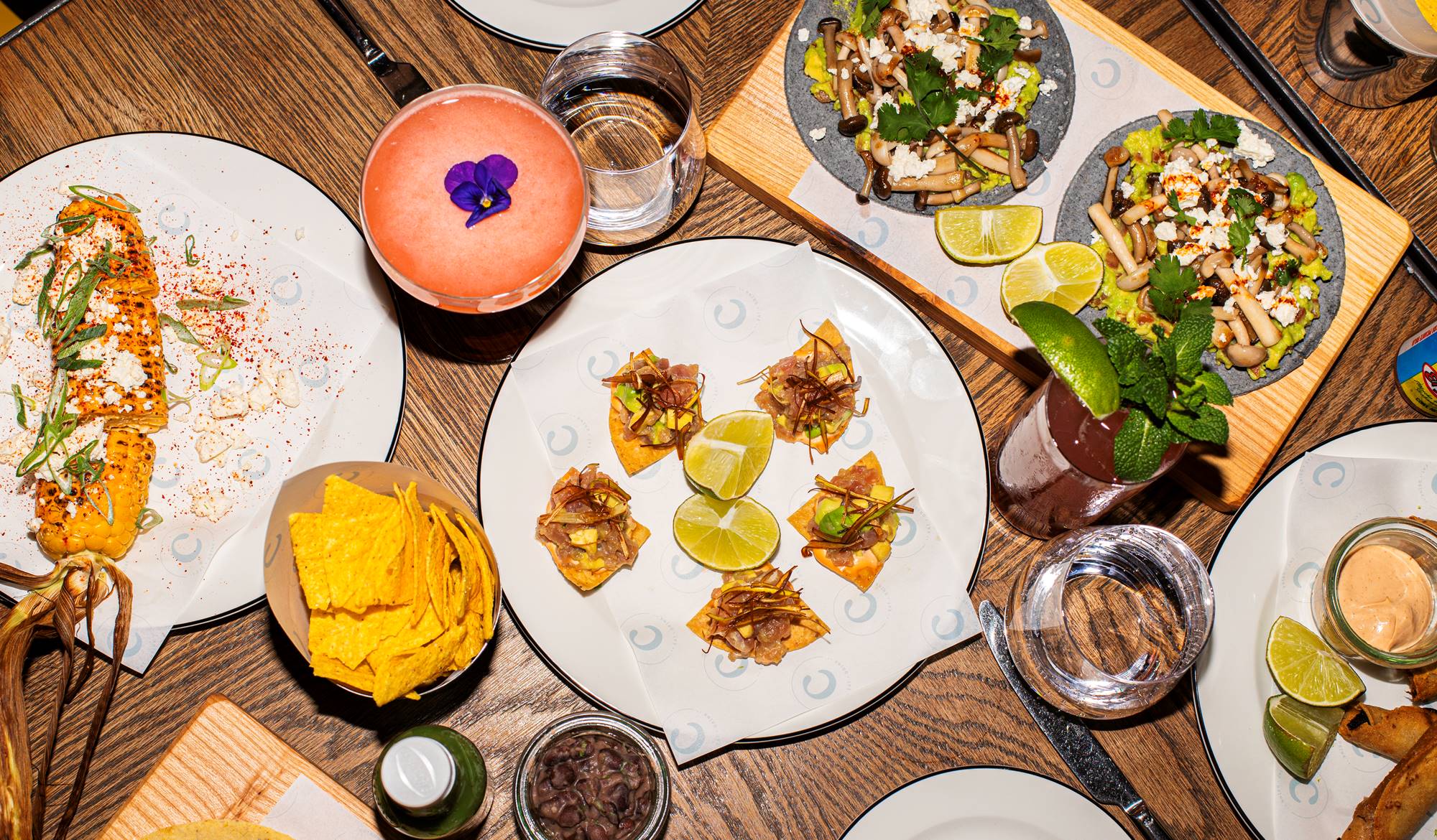 A variety of small bites, tacos, and cocktails on a table with lime wedges at Taco Tuesday at Celia in Amsterdam.