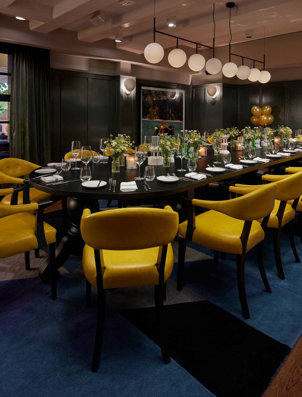 A dimly lit private dining room in Amsterdam with a large round table, yellow chairs, and floral arrangements at Celia.