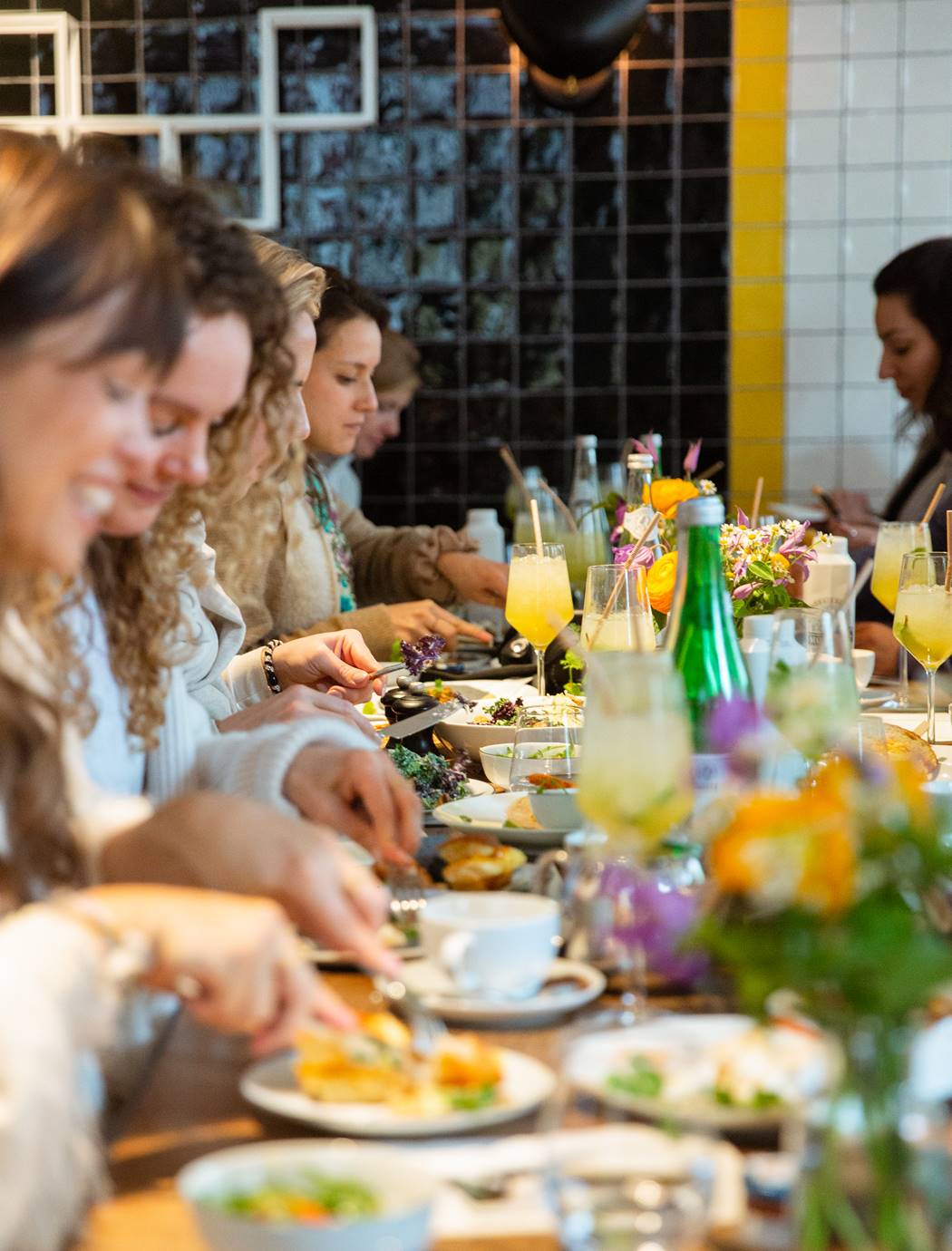 A long table filled with people eating brunch, with flowers and drinks in the center at Celia restaurant.