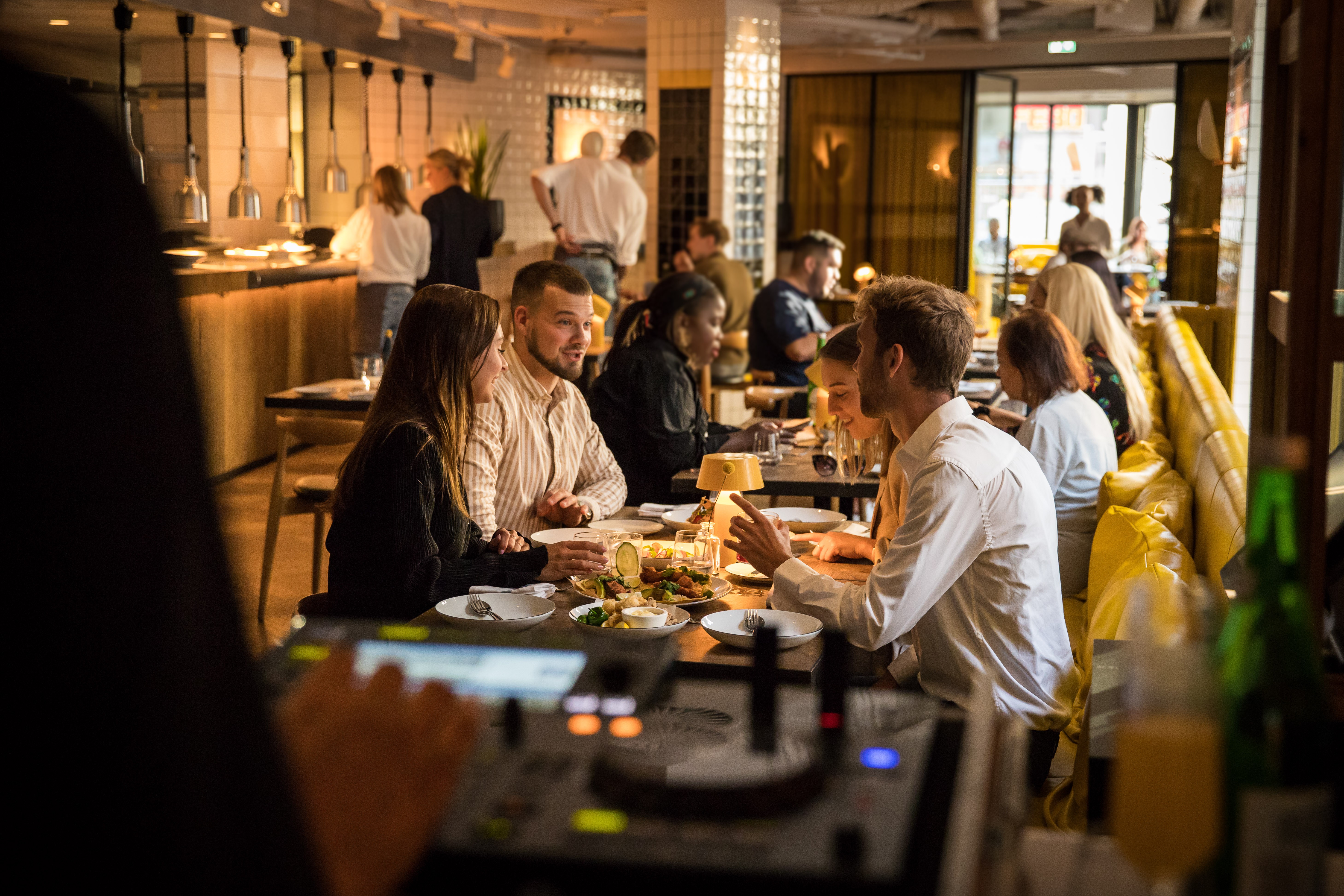 A DJ booth is visible in the foreground while diners chat and enjoy food at Celia's vibrant restaurant in central Amsterdam.