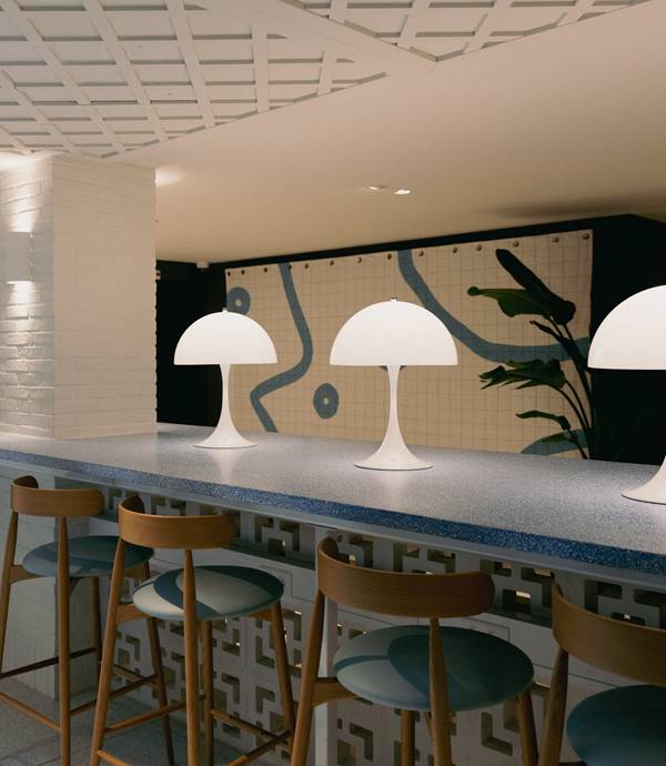 Modern bar with white lamps and wooden stools against a geometric tiled wall at Café Celia in Amsterdam.